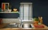 White horizontal Venetian blinds with blue fabric tapes, lowered and partially closed, filtering daylight through slats; kitchen sink with dark blue walls, wooden countertop, hex-tile backsplash, plants and utensils.
Text: LOVE
Text: JUICE
Text: ROSA'S THAI CAFE THE VEGETARIAN COOKBOOK
Text: CRAFT BEER