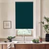 A dark teal roller blind is lowered over a kitchen window above a faucet and sink, with wooden cabinets, countertops holding bowls of greens, potted plants, and a framed sketch.