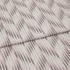 Folded patterned fabric with diagonal ikat-style stripes in muted taupe and blush lies folded across the frame, showing woven texture and subtle vertical lines in a studio-lit close-up.