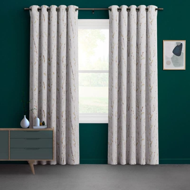 White grommet-top curtains with a subtle branch-and-leaf pattern, hanging slightly parted on a metal rod to reveal a sunlit window; dark teal room with a sideboard, vases, and framed abstract art.
