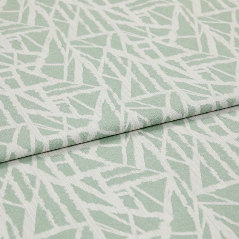 Folded pale green-and-white woven fabric with angular, leaf-like geometric pattern and subtle ribbed texture — overlapped across the frame — close-up on a flat, softly lit studio background.