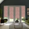 Patterned pink-and-white roller blinds cover four tall glass doors in a contemporary living room with green armchairs, a glass coffee table on a chevron rug, and a garden visible outside.