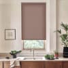 A brown roller blind covers most of a kitchen window above a stainless-steel sink; the countertop features a faucet, vegetable bowl, potted plants, a folded towel, and wood cabinetry beneath.
