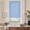 Blue roller blind hangs over a window above a stainless sink on a marble countertop in a kitchen with wooden cabinets, potted plants, a bowl of greens and a framed sketch.