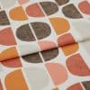 Printed fabric featuring repeated half‑circle motifs in orange, rust, beige and textured brown, folded once across the frame, photographed close-up on a neutral surface with soft, even lighting.