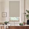 Beige roller blind lowered over a window, showing a sliver of foliage; stainless faucet and sink sit below on a marble countertop with potted plants and a bowl of greens.