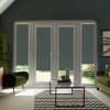 French doors with dark roller blinds covering glass panels, letting narrow light strips at the bottom; glass coffee table and chevron rug between green velvet armchairs in a living room.
