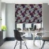 Floral Roman blind, lowered over patio doors with dense white, purple and red blooms; filtering soft daylight into a modern dining nook with a white tulip table, grey chairs, plant.