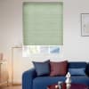 Light-green cellular pleated blind, lowered with horizontal folds and slightly raised at the bottom, filtering daylight in a modern living room with a blue sofa, floor lamp and small table.