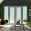 Glass patio doors with pale blue roller blinds covering the lower panes, framing a garden outside; flanked by green armchairs and a glass coffee table on a chevron rug in a modern living room.