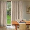 Beige-and-white patterned floor-length curtains, hung beside a tall black-framed window, are parted to reveal a green yard; wooden dining table with chairs sits in a sunlit, minimalist dining room.