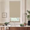 Beige roller blind covers most of a window above a kitchen sink; stainless faucet, wooden cabinets, countertop with bowls of leafy greens, potted plants, and a framed sketch nearby.