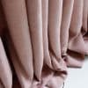 Textured pink curtains hang in deep vertical pleats, pooling on the floor; soft folds filter diffuse light, suggesting a softly lit interior space.