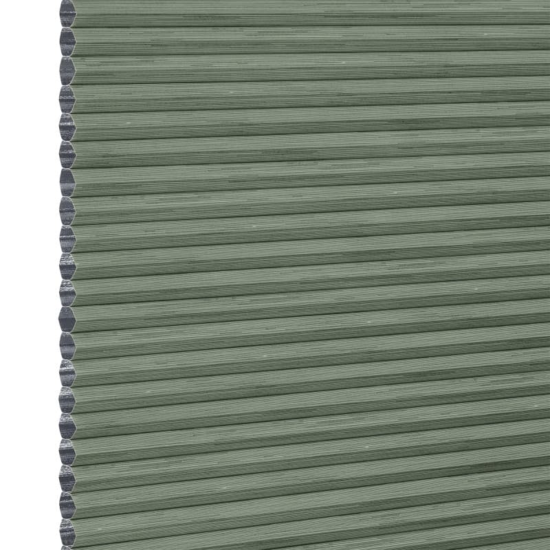 Cellular honeycomb blind — sage-green pleated fabric fully lowered with exposed hexagonal cells along the left edge; blocking and softly filtering light in a neutral interior.