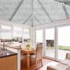 Pleated cellular blinds on the pitched conservatory roof and matching white pleated blinds on windows and patio doors, mostly lowered and filtering soft daylight; dining area opening onto a garden.