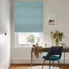 Light teal fabric Roman blind, fully lowered with horizontal folds, gently filtering daylight; home office with wooden desk, teal chair, vase of flowers and window view of trees.