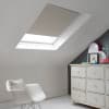 Room with white eaves wall, dark blue-grey wall to right with a shabby chic white drawer unit, a contemporary white chair, white painted floorboards and a skylight blind in pale grey with a subtle glitter effect.