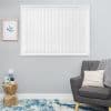 White vertical blinds covering a window, closed and diffusing light; grey armchair with knit throw and pale cushion, wooden stump side table, framed botanical print and blue-patterned rug.