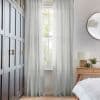 Sheer floor-length curtains, light gray and pleated, hung at a tall sash window; they filter soft daylight and are parted, in a bedroom with dark paneled wardrobe and wooden nightstand.