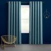 Teal grommet-top curtains, full-length panels on a metal rod, drawn slightly apart and filtering light from a window; navy-painted room with gray carpet, brass wire chair and circular wall sconce.