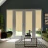 French glass patio doors with beige roller blinds lowered, filtering daylight; set in a living room framed by green upholstered chairs, chevron rug, glass coffee table and potted plants.