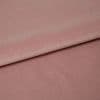 Dusty-rose velvet fabric folded across the frame, overlapping with a visible crease; its nap catches soft highlights in a close-up studio view on a flat surface.