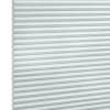 Pleated honeycomb blind, pale gray-blue with hexagonal cells along the left edge, fully lowered and closed, softly filtering daylight, set against a bright white background in a neutral-lit interior.