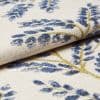 Cream woven curtain fabric with raised blue floral motifs and gold-thread stems — folded and layered, showing textured weave — close-up studio-lit textile sample with soft, neutral background.