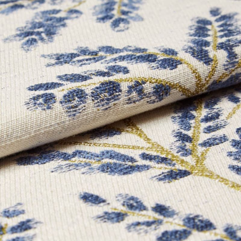 Cream woven curtain fabric with raised blue floral motifs and gold-thread stems — folded and layered, showing textured weave — close-up studio-lit textile sample with soft, neutral background.
