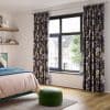 Floral-patterned pleated curtains, pulled to either side and framing a black-framed casement window, filtering bright daylight into a modern bedroom with wooden floor, bed and green round pouf.