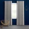 Gray, textured grommet-top curtains, floor-length and evenly pleated, hang on a metal rod flanking a centered window, slightly parted to admit daylight, set against a deep-blue wall with gold accents.
