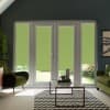 French glass patio doors with lime-green roller blinds lowered halfway, overlooking a sunlit garden; living room with green armchairs, glass coffee table and black-and-white chevron rug.