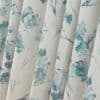 Fabric curtains with vertical pleats and teal watercolor floral print, hanging in soft folds; close-up interior view with neutral cream background and diffuse natural light.