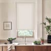 Light gray roller blind covers upper window, filtering daylight; stainless faucet rises above double sink; countertop displays bowl of greens, potted plants and draped towel in a modern kitchen.