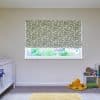 Patterned roller blind (white with green squiggly pattern) lowered over window, filtering daylight into a simple nursery with a white crib at left and a plush orange octopus by a toy shelf.