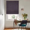 Roman fabric blind, deep plum, lowered with soft folds near the bottom; filtering daylight. Context: small home study — wooden desk with mirror, vase of foliage, teal-upholstered chair and wall art.