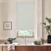 Roller blind covers a kitchen window, blocking light; stainless faucet and double sink sit below on a marble countertop with wooden cabinets, potted plants, a bowl of vegetables, and framed sketch.