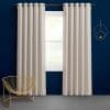 Cream grommet-top curtains, hung on a metal rod and parted to reveal a central window, filtering soft daylight; set against a deep navy wall with a gold wire chair.