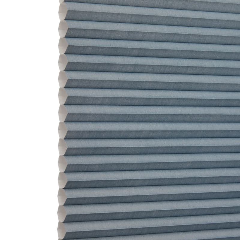 Blue-gray honeycomb (cellular) blind, fully lowered with horizontal pleats and visible hexagonal cells at the left edge; blocking light and insulating; shown close-up against a neutral, softly lit background.