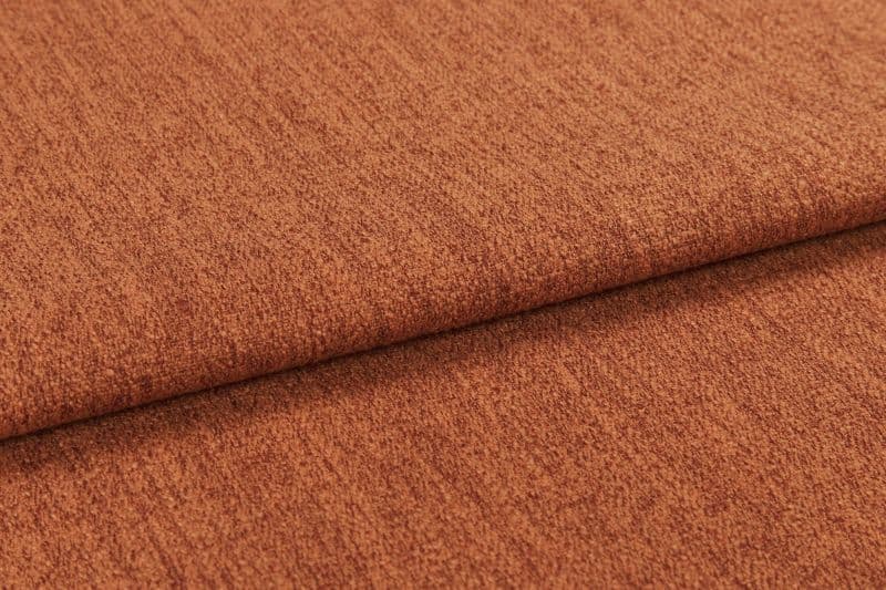 Burnt-orange textured fabric (upholstery cloth) folded once, overlapping edge casting a soft shadow; close-up studio view highlighting its nubby weave and warm, evenly lit surface.