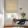 Beige patterned Roman blind pulled down over a white-framed window, softly filtering daylight; below, a wooden desk with mirror, vase of flowers and teal chair in a bright, neutral home office.