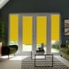 Double glass patio doors covered by bright yellow roller blinds pulled down over lower panes in a modern living room with green armchairs, glass coffee table, chevron rug and plants.