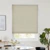 Light-beige cellular blind, fully lowered with horizontal pleats, filtering daylight; modern dining room with round table, vase and glassware, potted fiddle‑leaf fig visible by the window.