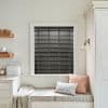 Black horizontal slatted blinds, fully lowered and closed with visible ladder tapes, blocking light; set in a white‑trimmed window above a cushioned window seat in a softly lit neutral kitchen.