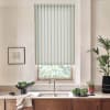 Striped roller blind lowers over a window, filtering light. In a kitchen setting, stainless faucet over a double sink, countertop with bowls of greens, a potted plant, and framed sketch.