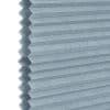 A light-blue honeycomb (cellular) blind, hexagonal cells visible along the left edge; closed into uniform horizontal pleats, blocking view and filtering light, shown in a close-up with soft, neutral lighting.