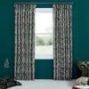 Black-and-white wavy-striped pleated curtain panels, hung on a metal rod and parted, framing the central window and admitting daylight into a teal-walled room with cushions and a green leather armchair.