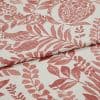 Cream fabric printed with terracotta botanical and pomegranate motifs, folded and overlapped to show pattern repeat, close-up on a flat surface under soft, even studio lighting.