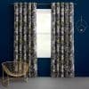 Floor-length grommet-top floral curtains, dark gray with white and lime blossoms, parted on a rod to filter daylight through a central window; navy room with gold chair and circular sconce.