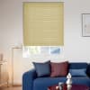 A pale-yellow pleated cellular blind, lowered to cover most of the tall window with a narrow lower gap, filtering daylight in a bright living room above a blue sofa.